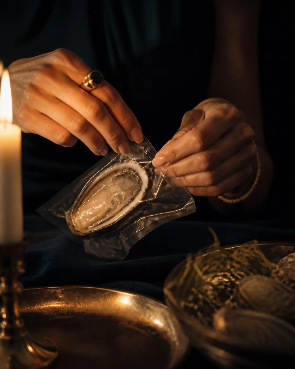 Hands opening a vacuum sealed pearl pouch by candlelight